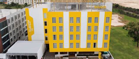 Un hotel moderno con fachada amarilla, varios pisos y una terraza en la azotea.