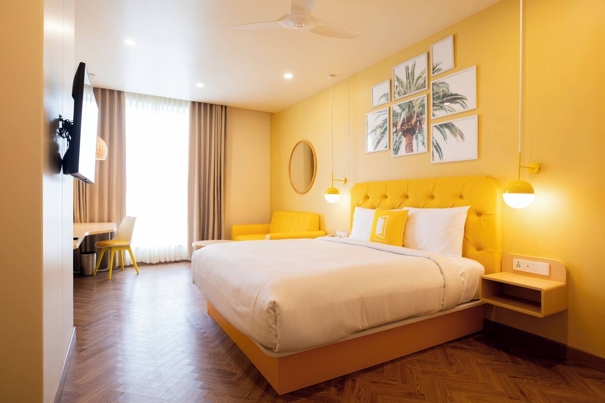 A hotel room with a large bed, a desk, and a chair. There are wall-mounted lights and a ceiling fan.