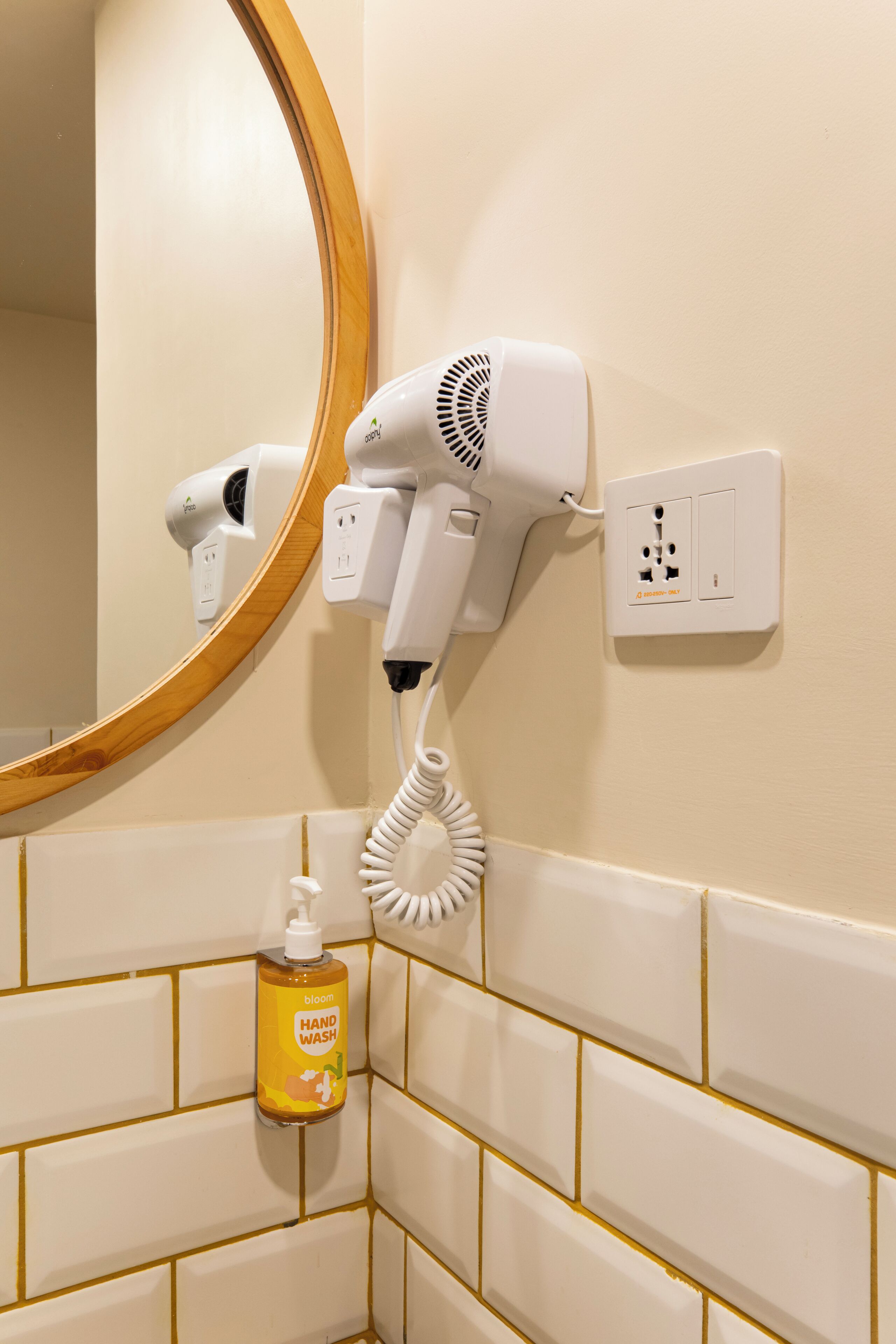 Une salle de bain équipée d’un sèche-cheveux fixé au mur, d’un distributeur de gel hydroalcoolique et d’un miroir avec un cadre en bois.