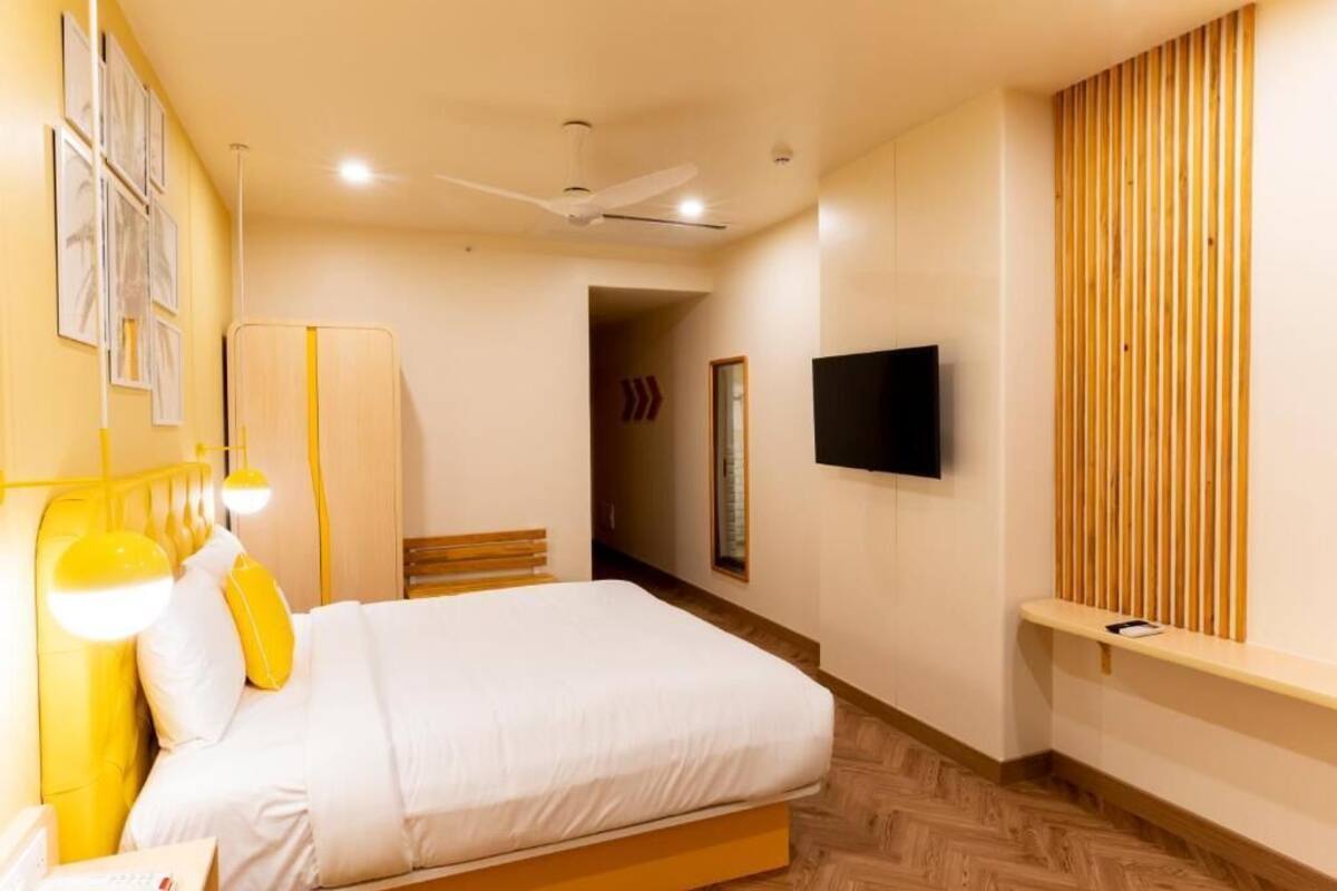 A bedroom with a bed, bedside table, lamp, TV, and wooden panel wall.