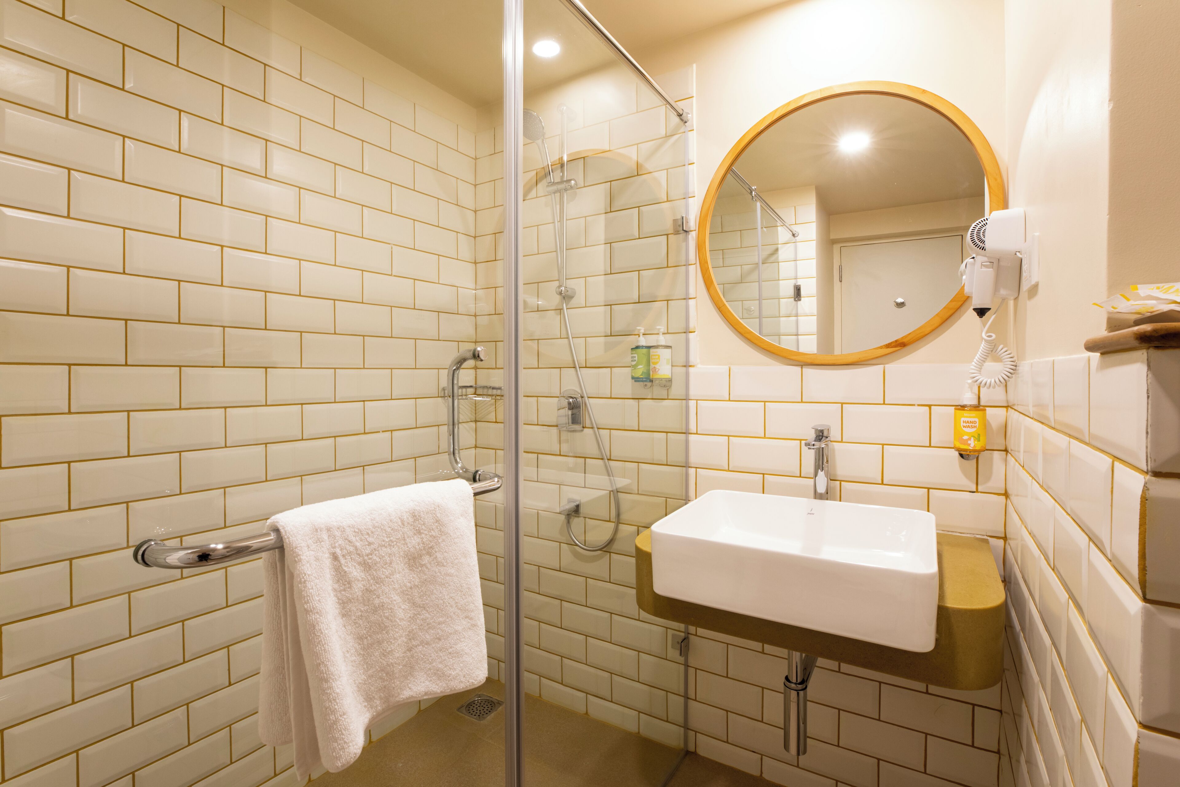 Un baño con ducha acristalada, un lavabo blanco y un espejo redondo.