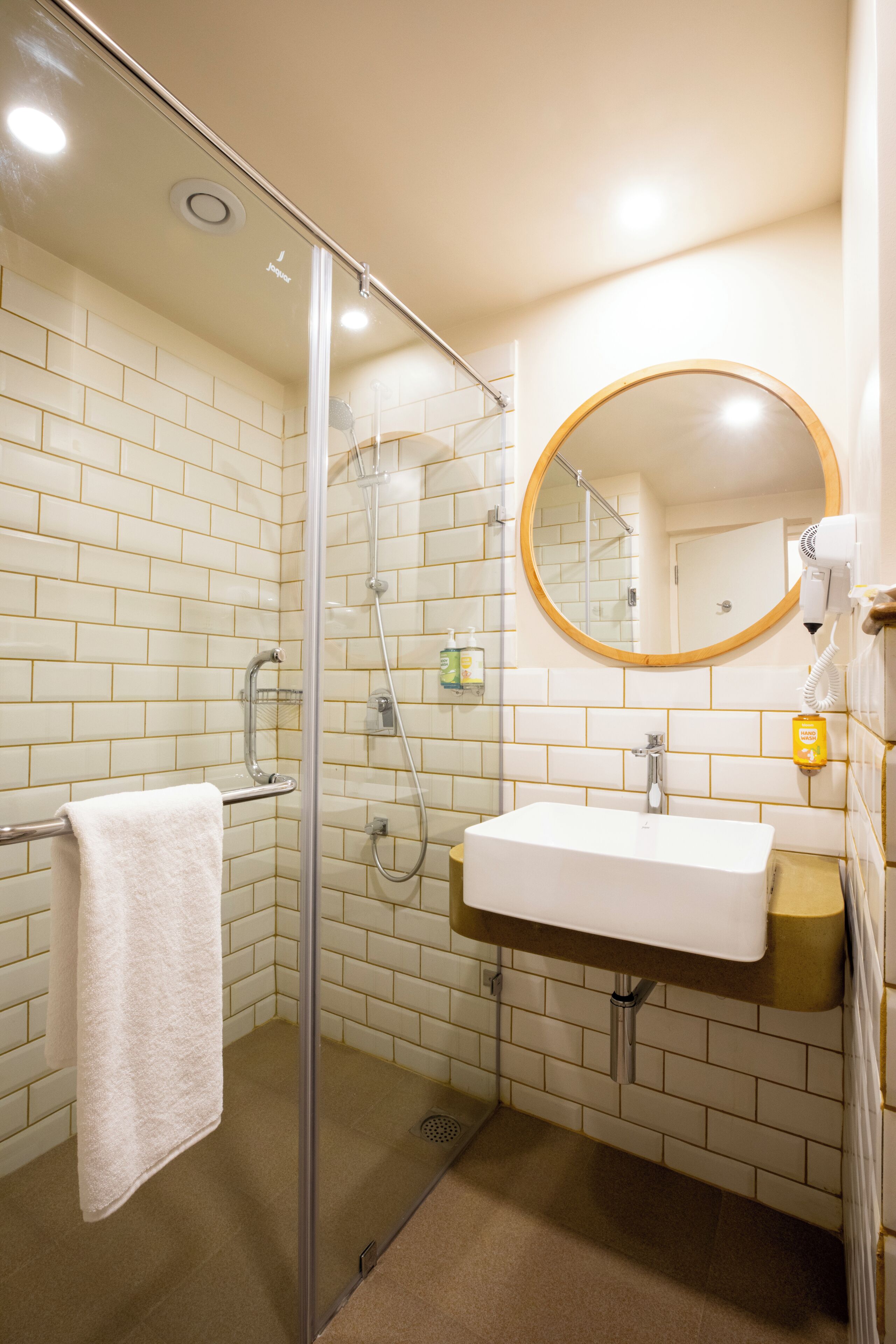 A modern bathroom with a glass shower enclosure, a white sink, and a round mirror.