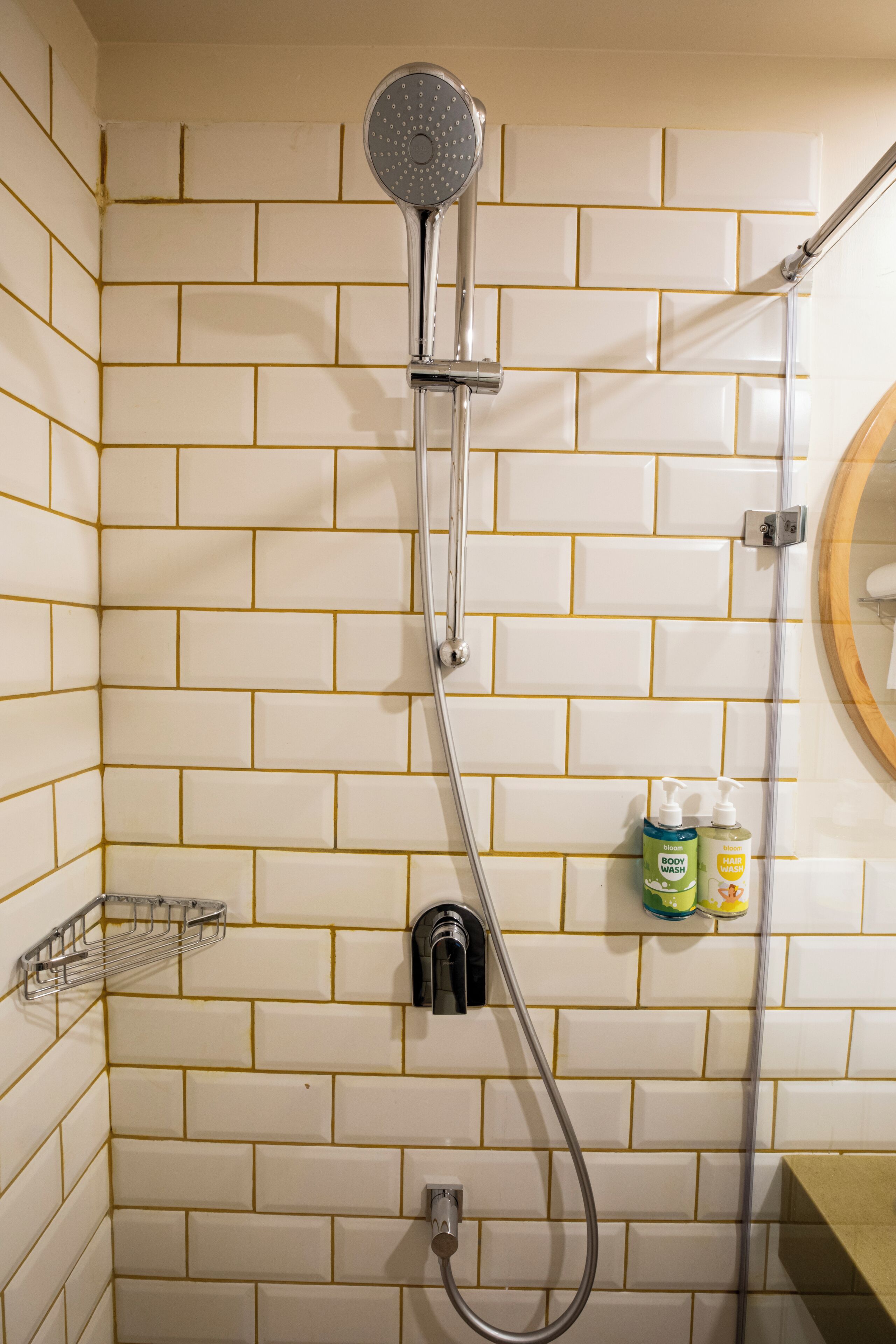 Un baño con paredes de azulejos blancos, cabezal de ducha, ducha de mano y dispensador de jabón en la pared.