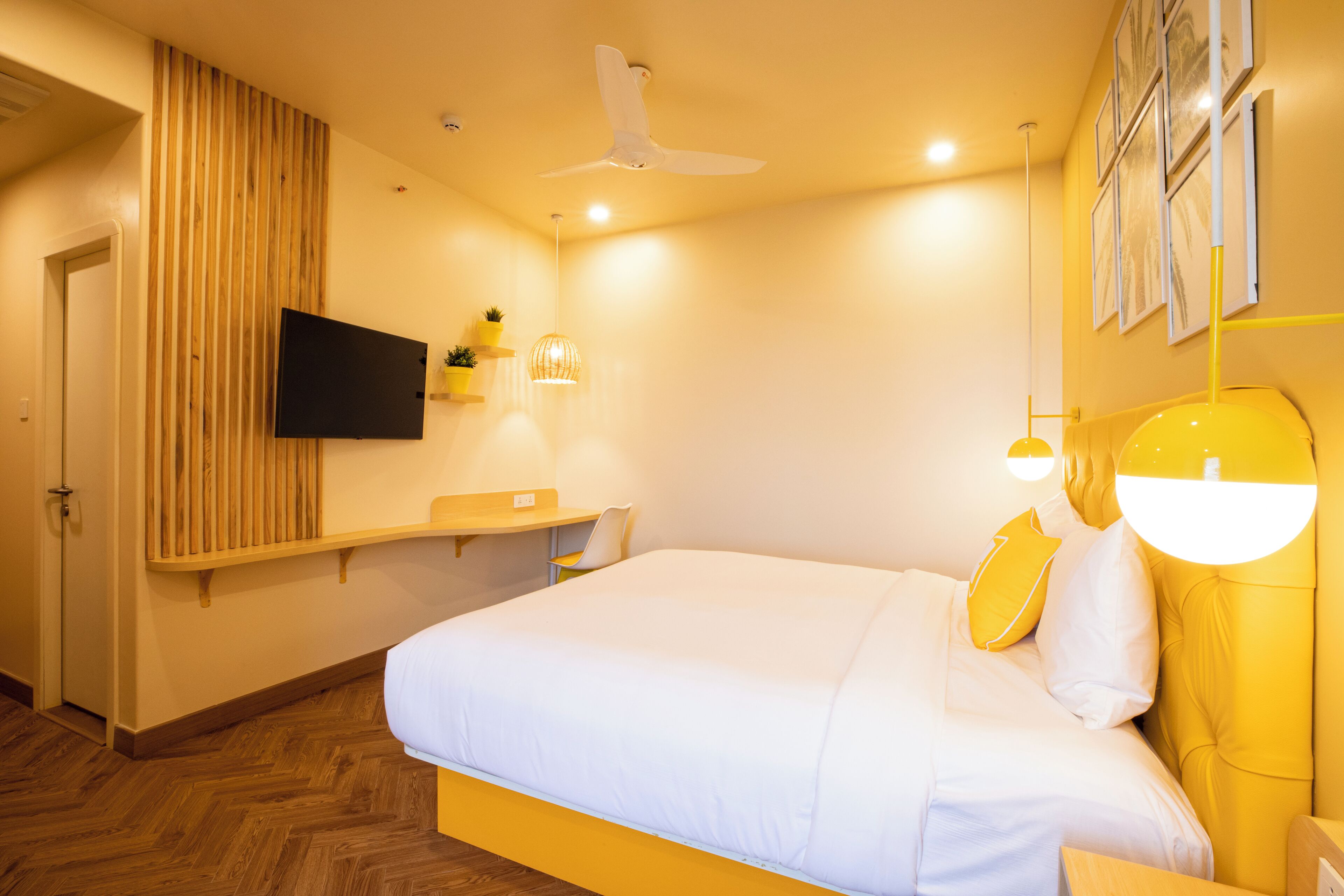 Une chambre d’hôtel équipée d’un lit, d’un téléviseur fixé au mur, d’un ventilateur de plafond et d’un mur recouvert de panneaux de bois.