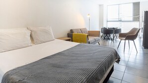 A modern hotel room with a large bed, a small sofa, a desk, and a dining area with chairs. - Urban Loft: Style and Comfort (Medellín)