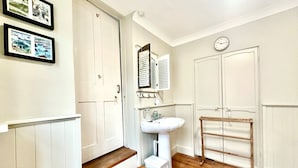 A bathroom with a wooden floor, white walls, a sink, a mirror, and two doors. - Zeta Cottage - Ryde, Isle of Wight (Ryde)