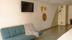 Une pièce avec un canapé de couleur turquoise, un téléviseur fixé au mur et une porte dotée d’un porte-serviettes.