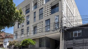Ein modernes Gebäude mit einer markanten, perforierten Fassade, zahlreichen Fenstern und einer darunterliegenden Straße.