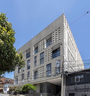 A modern building with a unique perforated facade, multiple windows, and a visible street below. - Queen bed and street view! (Medellín)