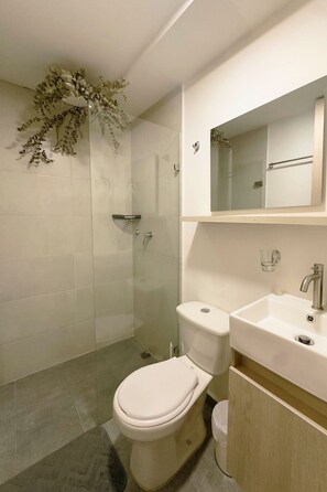 A modern bathroom with a toilet, sink, and shower. - Queen bed and street view! (Medellín)