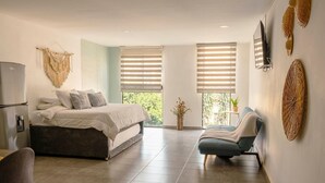 Ein modernes Schlafzimmer mit einem Bett, einem Sessel, einem Fernseher und einem großen Fenster.