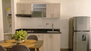 Une cuisine compacte équipée d’un four à micro-ondes encastré, d’un réfrigérateur en acier inoxydable et d’un coin repas avec une table et des chaises.