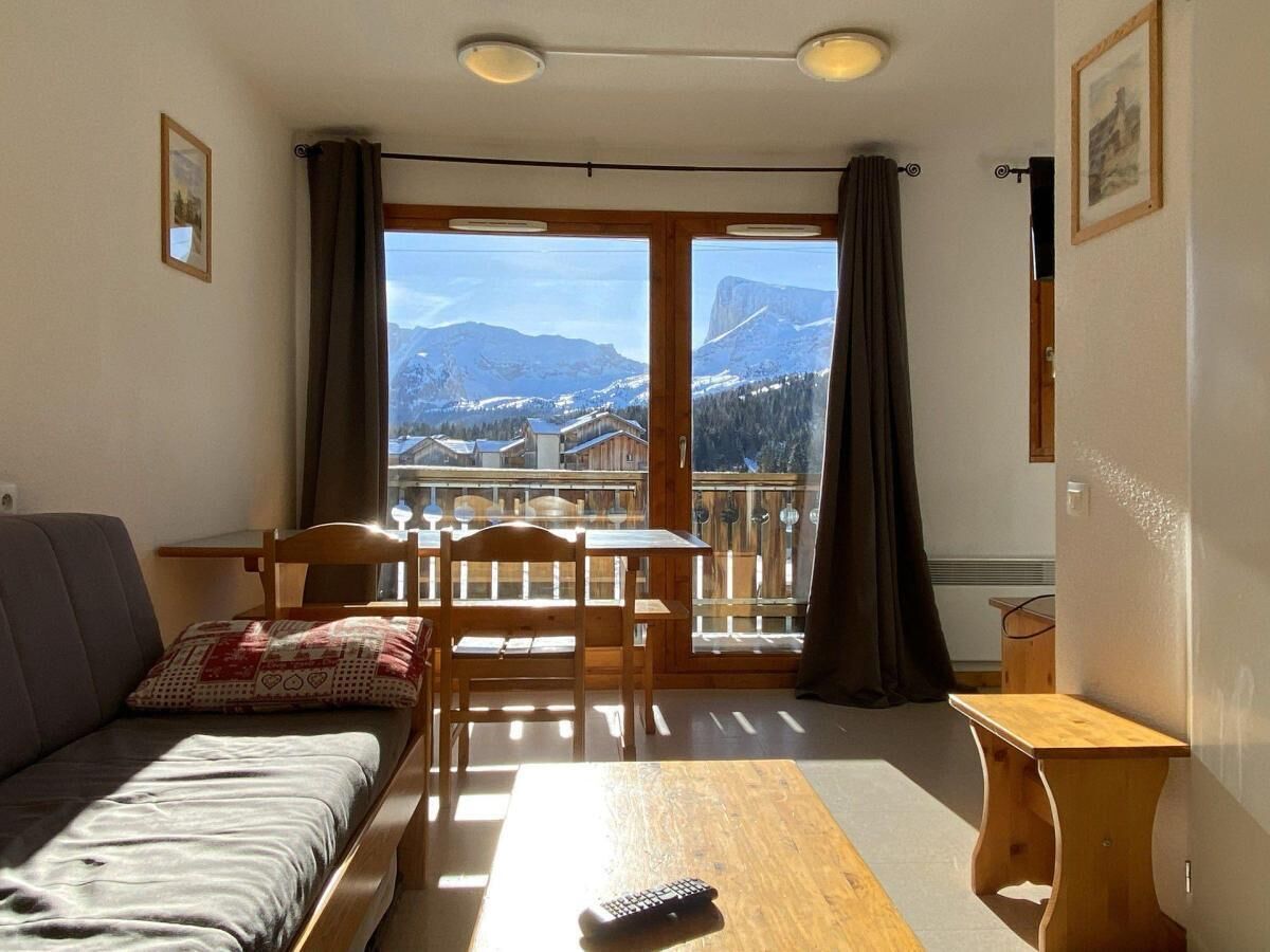 Ein gemütliches Zimmer mit einer Couch, einem Tisch und einem Sessel. Ein Fenster bietet Blick auf die Berge.
