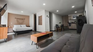 A modern living room with a sofa, a bed, a wooden coffee table, and a kitchen area in the background. - Large spaces, unique location (Medellín)