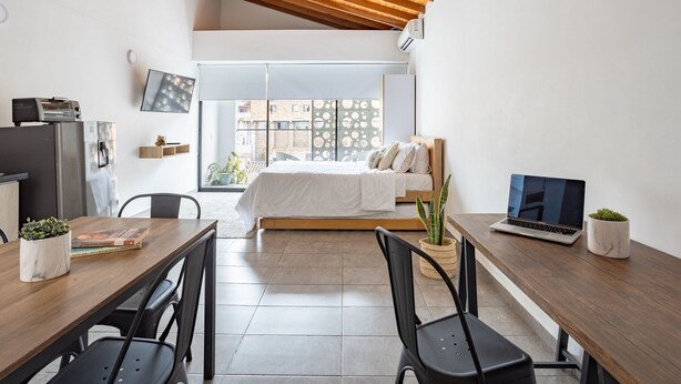 A modern, well-lit room with a wooden ceiling, a bed with a white duvet, a laptop on a desk, and a dining table with chairs. - AC loft/safe/Downtown (Medellín)