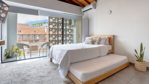 A bedroom with a large window, a bed, a potted plant, and a view of buildings outside. - AC loft/safe/Downtown (Medellín)