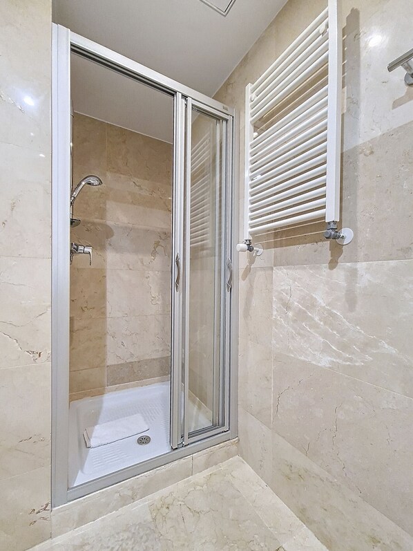 A modern bathroom with a glass-enclosed shower, a white towel rack, and marble walls.