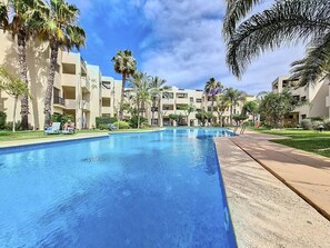 A swimming pool surrounded by palm trees and a building with balconies.