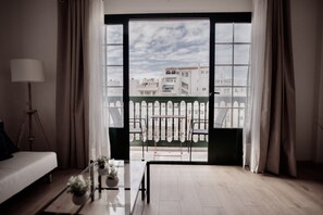 A room with a large window, a sofa, a small table with a plant, and a tripod lamp. - Moderno Apartamento en Puerto de Lacruz (Puerto de la Cruz)