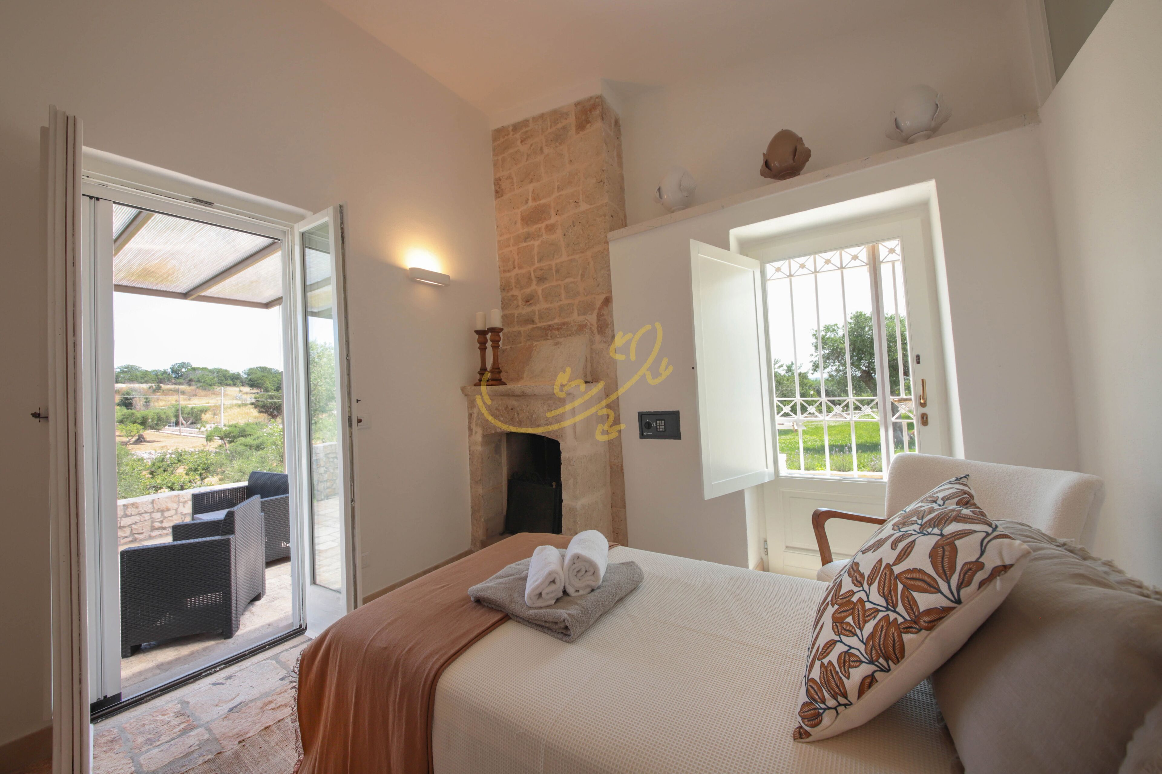 Ein Schlafzimmer mit Bett, Fenster, Kamin und Blick ins Freie.