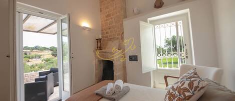 Ein Schlafzimmer mit Bett, Fenster, Kamin und Blick ins Freie.