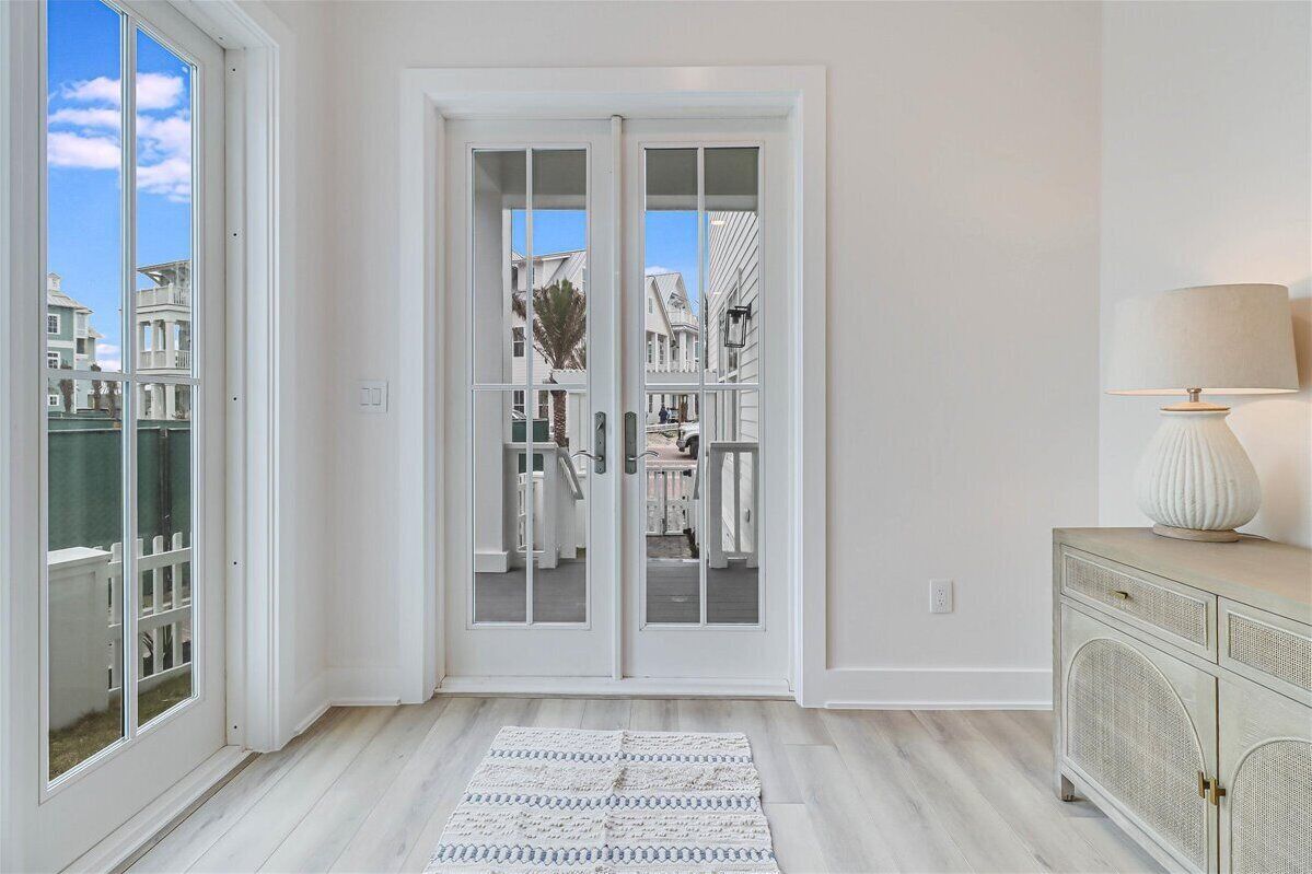 A room with a large sliding glass door leading to a balcony, a white cabinet with a lamp, and a patterned rug on the floor.