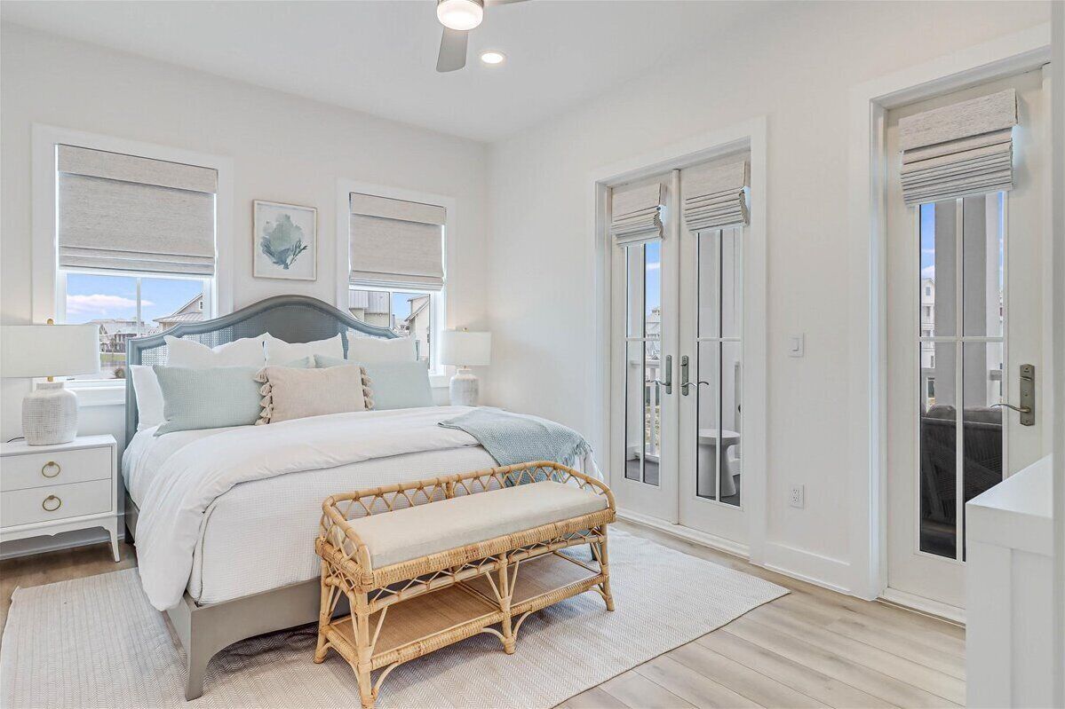 Quarto com cama, mesas de cabeceira, um banquinho, janela com persianas e porta com vista.