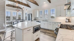 A modern kitchen with white cabinetry, a central island with seating, and pendant lighting. - Sea Ya at the Beach 237 MA (Port Aransas)
