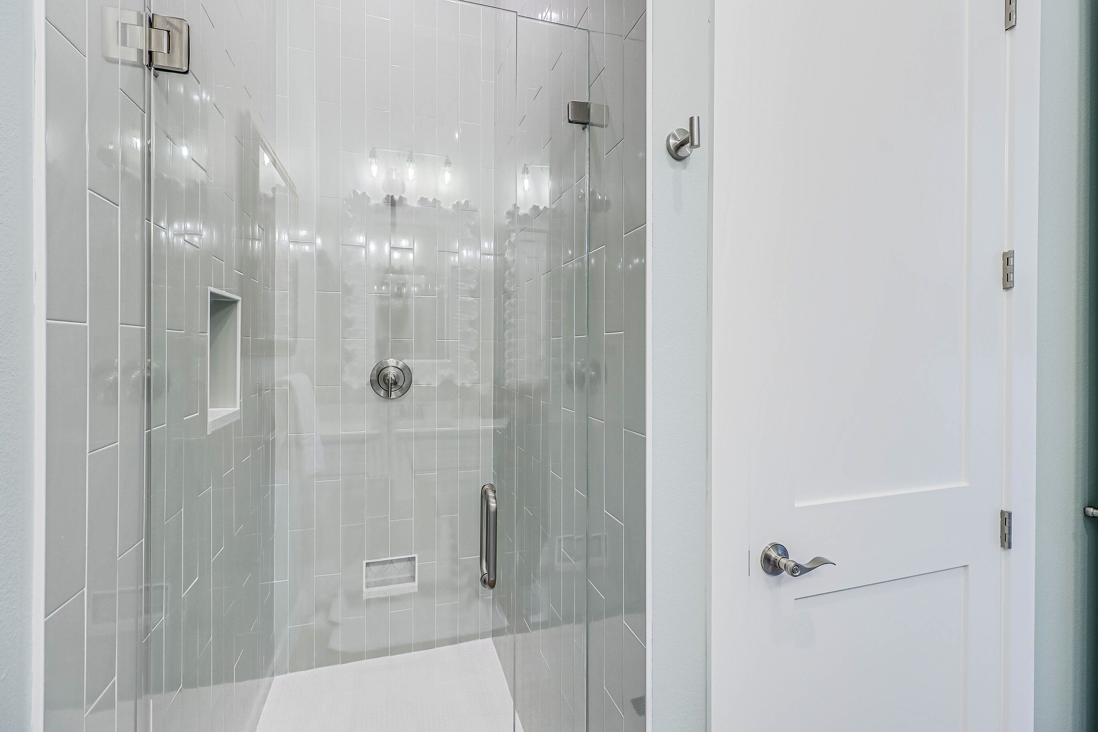 A modern bathroom with a glass shower enclosure, a white sink, and a door with a silver handle.