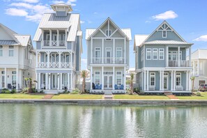 Houses with symmetrical design and central entrance, flanked by windows and a balcony, overlook a serene water feature.