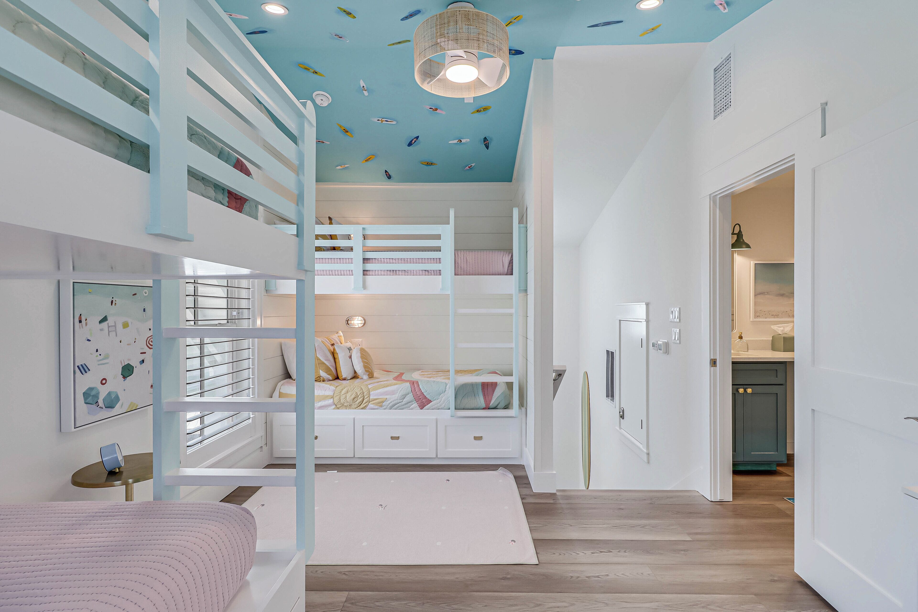 Une chambre d’enfant avec des lits superposés, un plafond décoré d’autocollants représentant des poissons, et un coin cuisine visible à travers une porte ouverte.