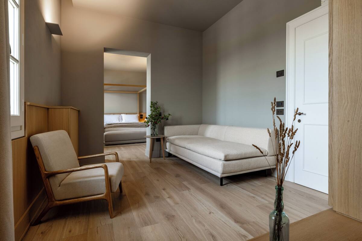 A modern living room with a sofa, armchair, and a small table with a vase.