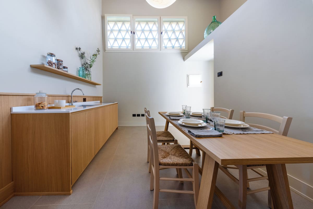 A compact kitchen with wooden cabinets, a dining table set for four, and a window with a grid pattern.
