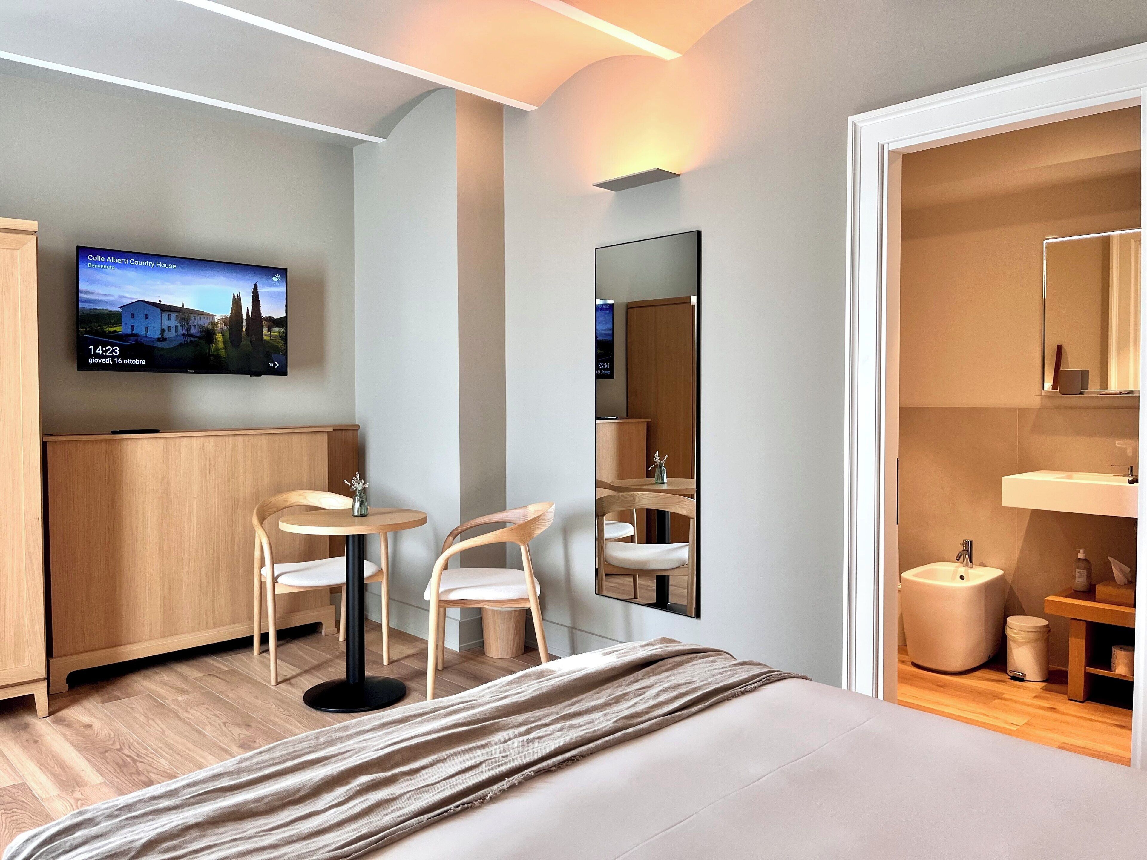 Ein Hotelzimmer mit Bett, Fernseher, Schreibtisch mit zwei Stühlen, Spiegel und einem Badezimmer mit Waschbecken und Toilette.