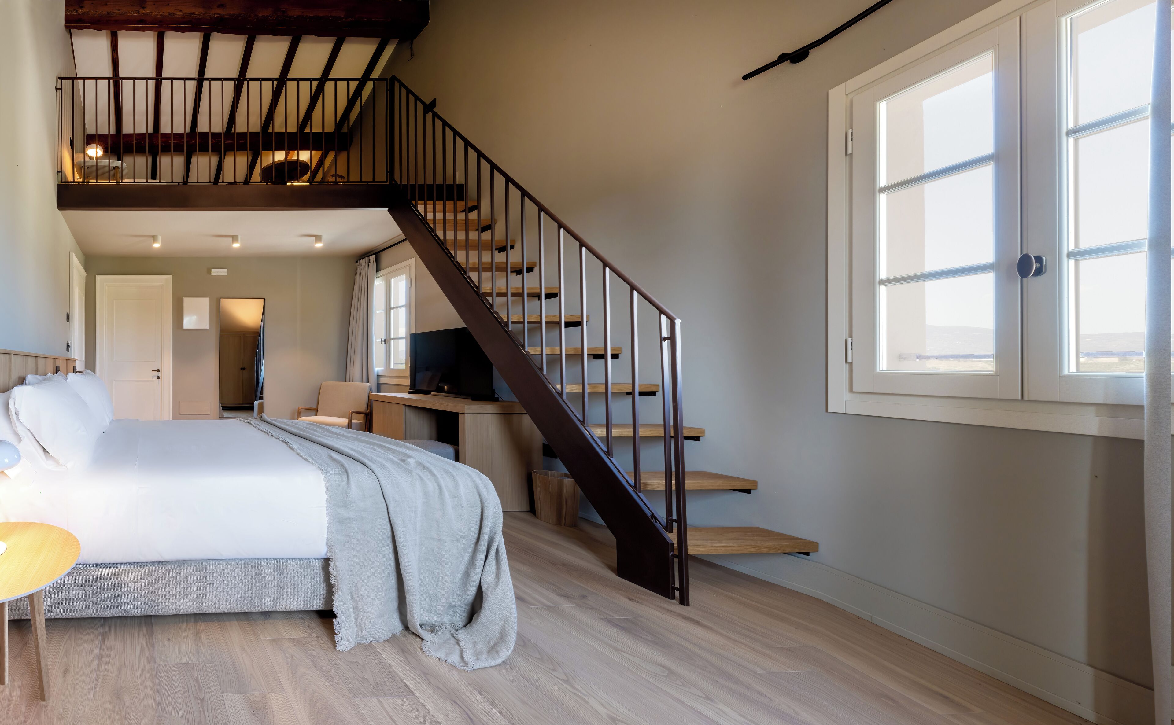 Ein Schlafzimmer mit Bett, Schreibtisch, Stuhl, Fernseher, Treppe und Fenster.