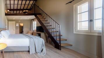 Ein Schlafzimmer mit Bett, Schreibtisch, Stuhl, Fernseher, Treppe und Fenster.
