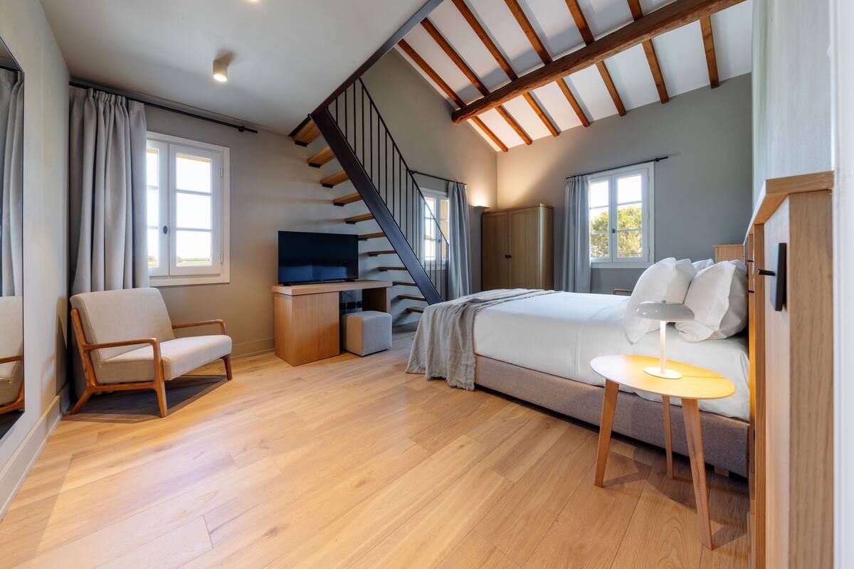 A modern bedroom with a bed, a desk, a chair, and a staircase.