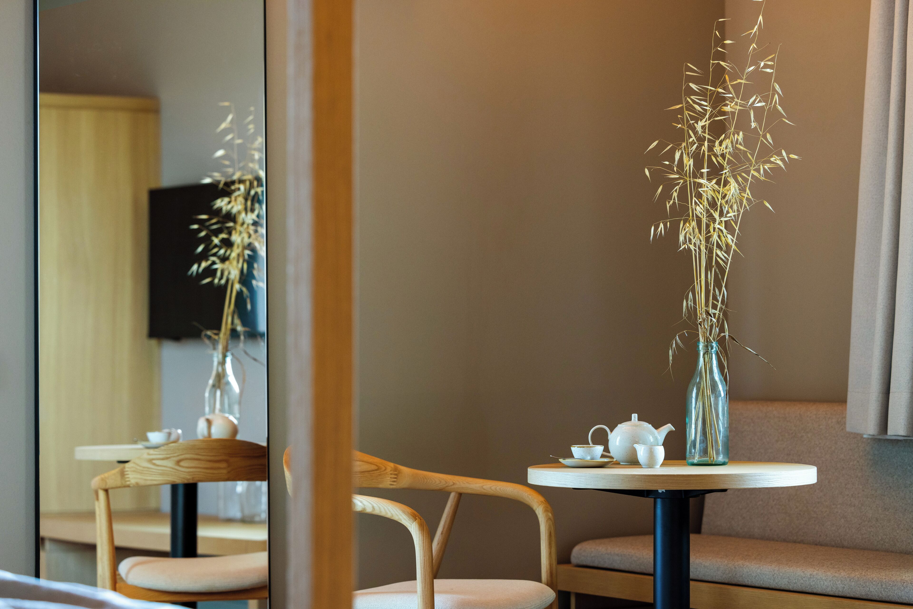 A room with a round table, two chairs, a vase with dried plants, a teapot, and a cup.