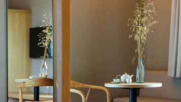 A room with a round table, two chairs, a vase with dried plants, a teapot, and a cup.