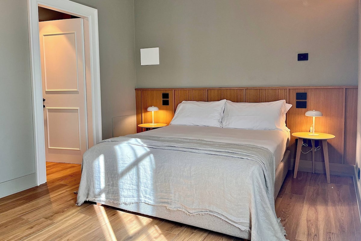 A neatly made bed with a wooden headboard, two bedside lamps, and a door to the left.