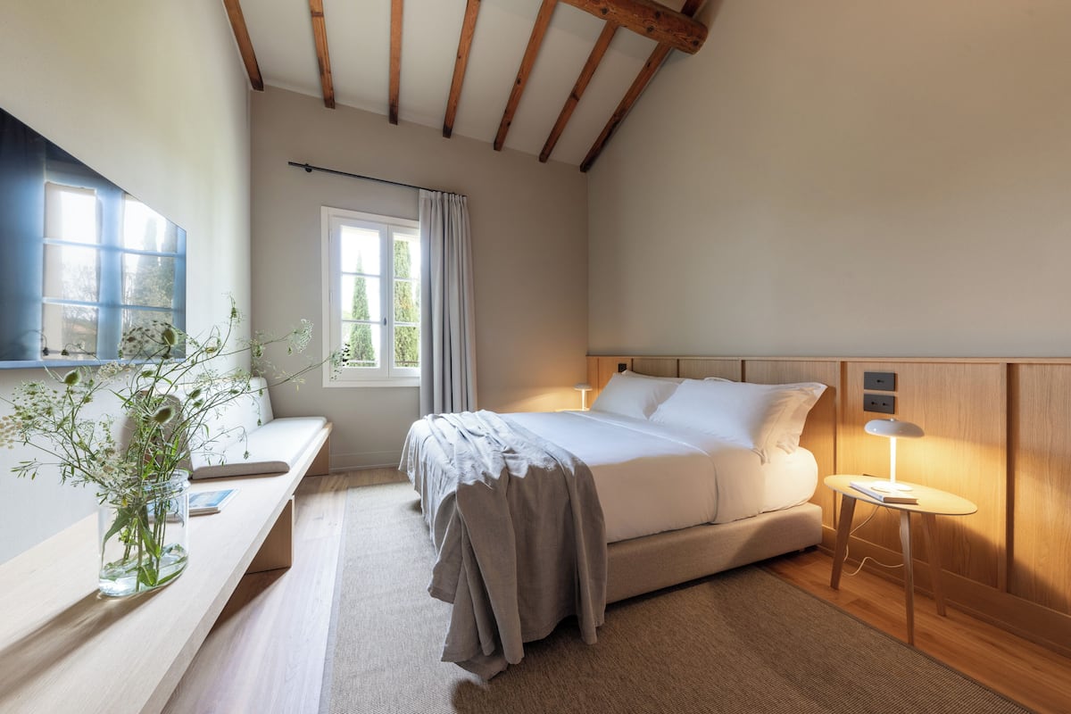 A bedroom with a bed, bedside table, lamp, and a window with curtains.