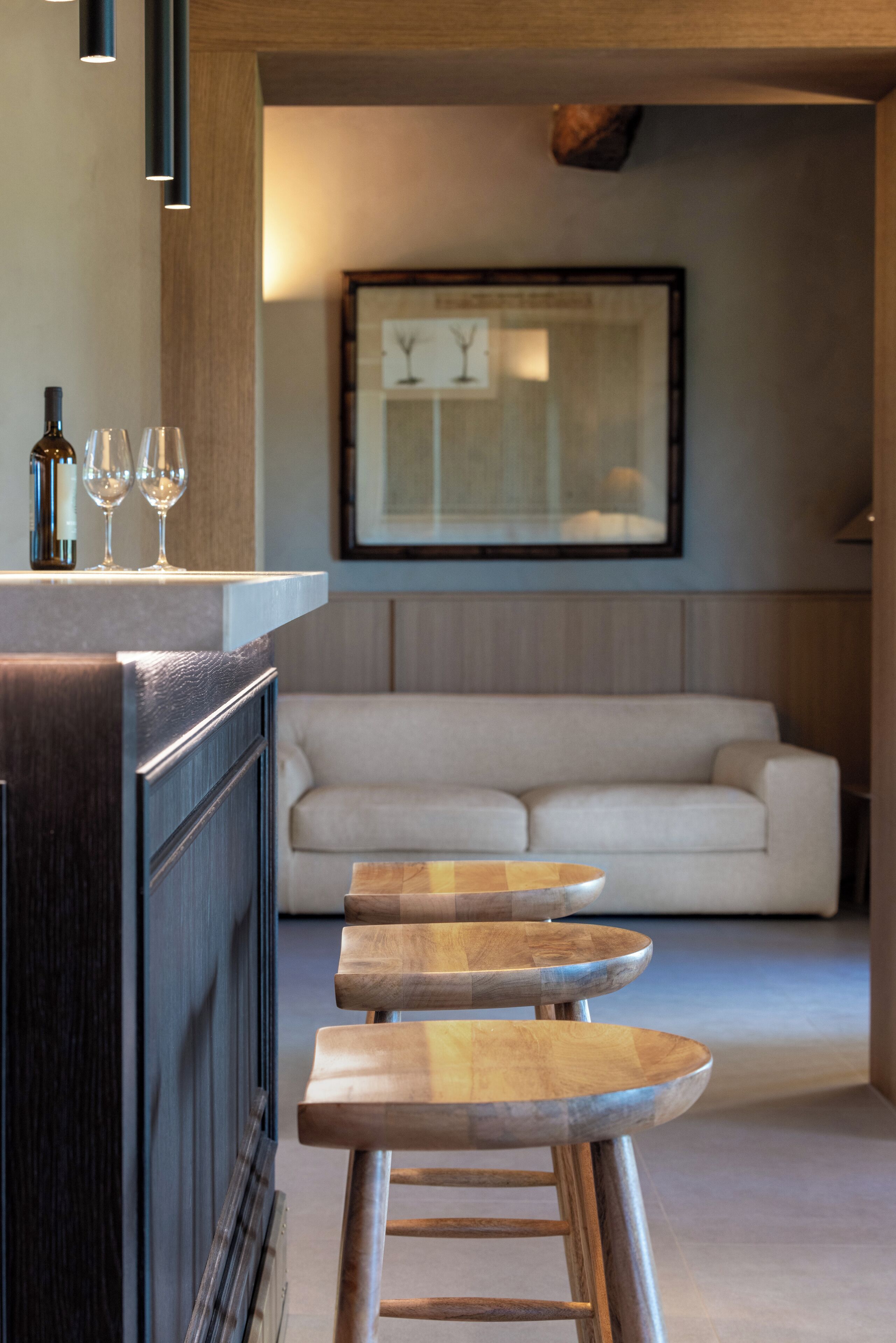 Cozinha moderna com área de bar, banquetas de madeira e um sofá ao fundo.