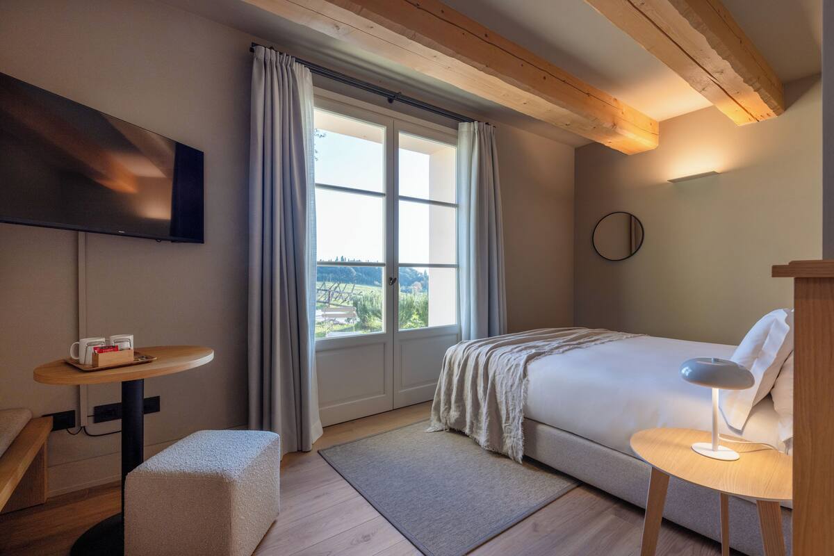 A hotel room with a bed, a desk, a chair, a TV, and a window with curtains.
