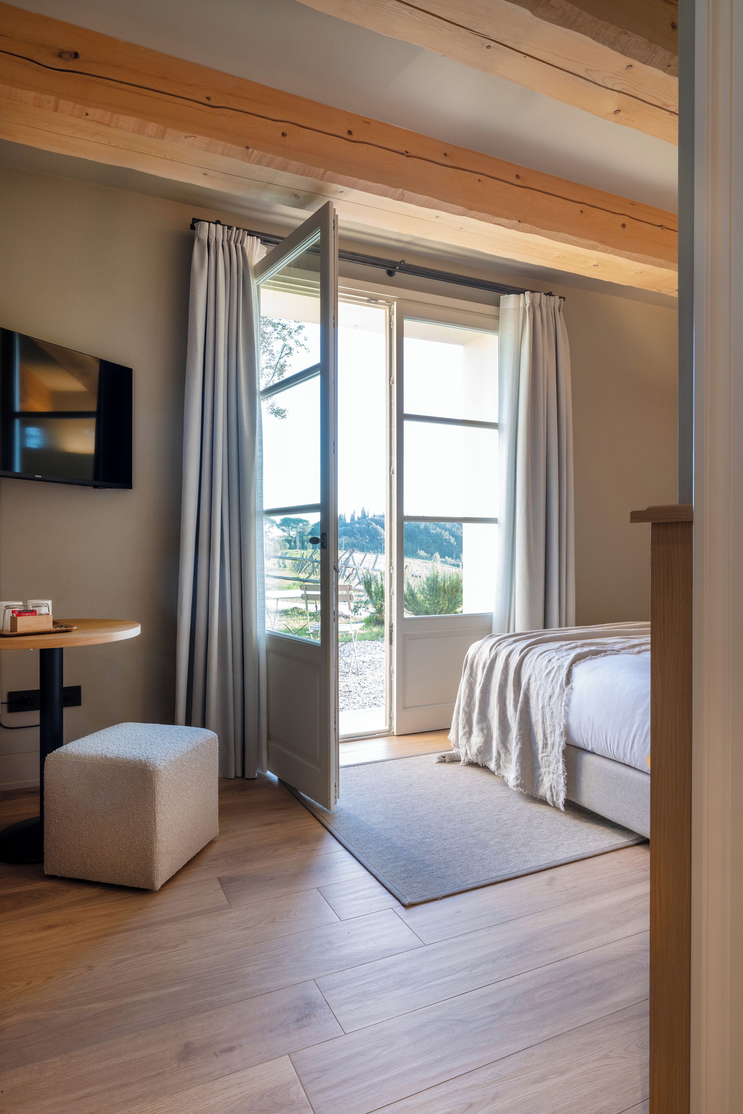 Une chambre à coucher avec un lit, un bureau, une télévision et une fenêtre avec des rideaux.