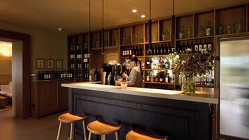 Eine Bar mit Holzregalen voller Flaschen, einer Theke mit Hockern und einer dekorativen Vase mit Blumen.