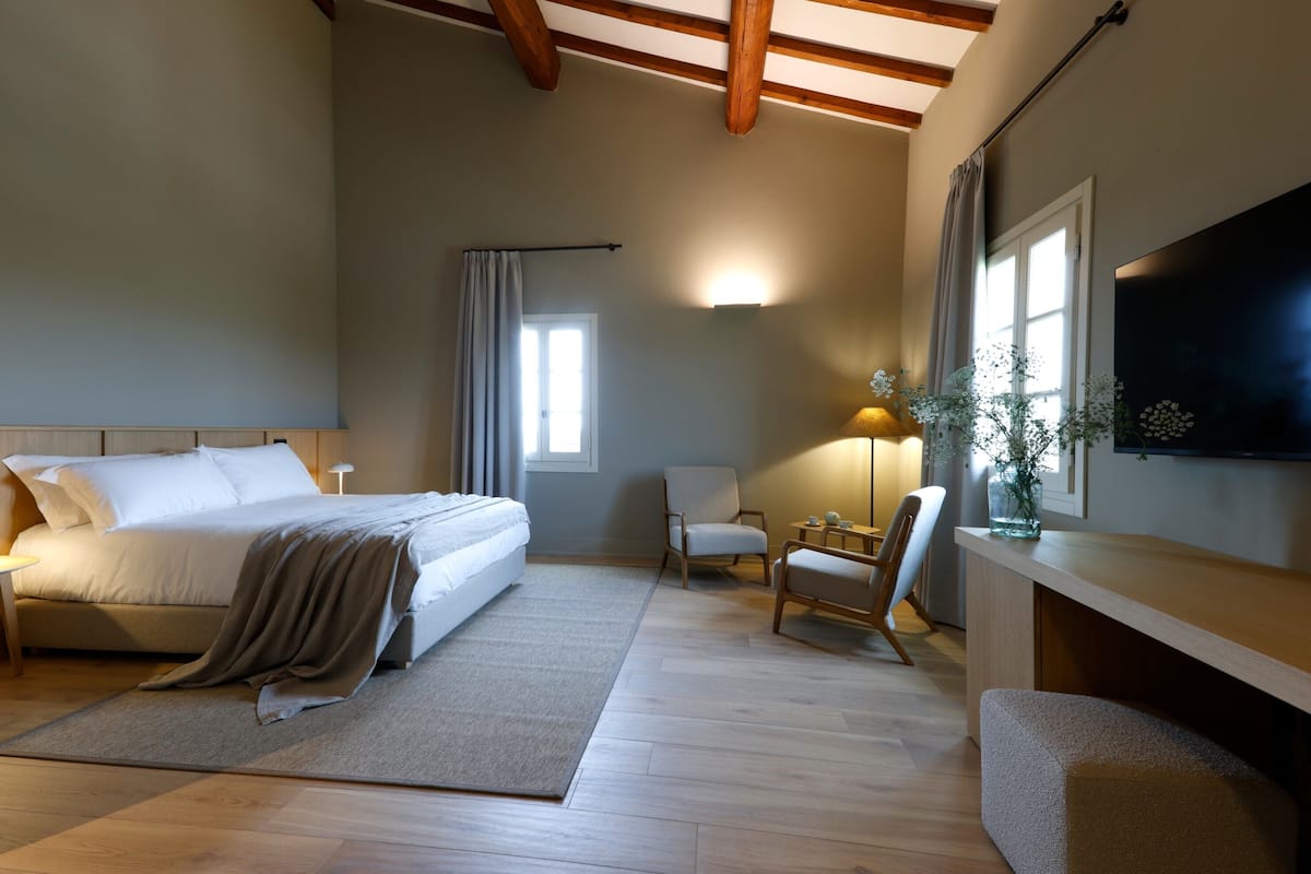 A bedroom with a bed, a desk, a chair, a TV, and a window.