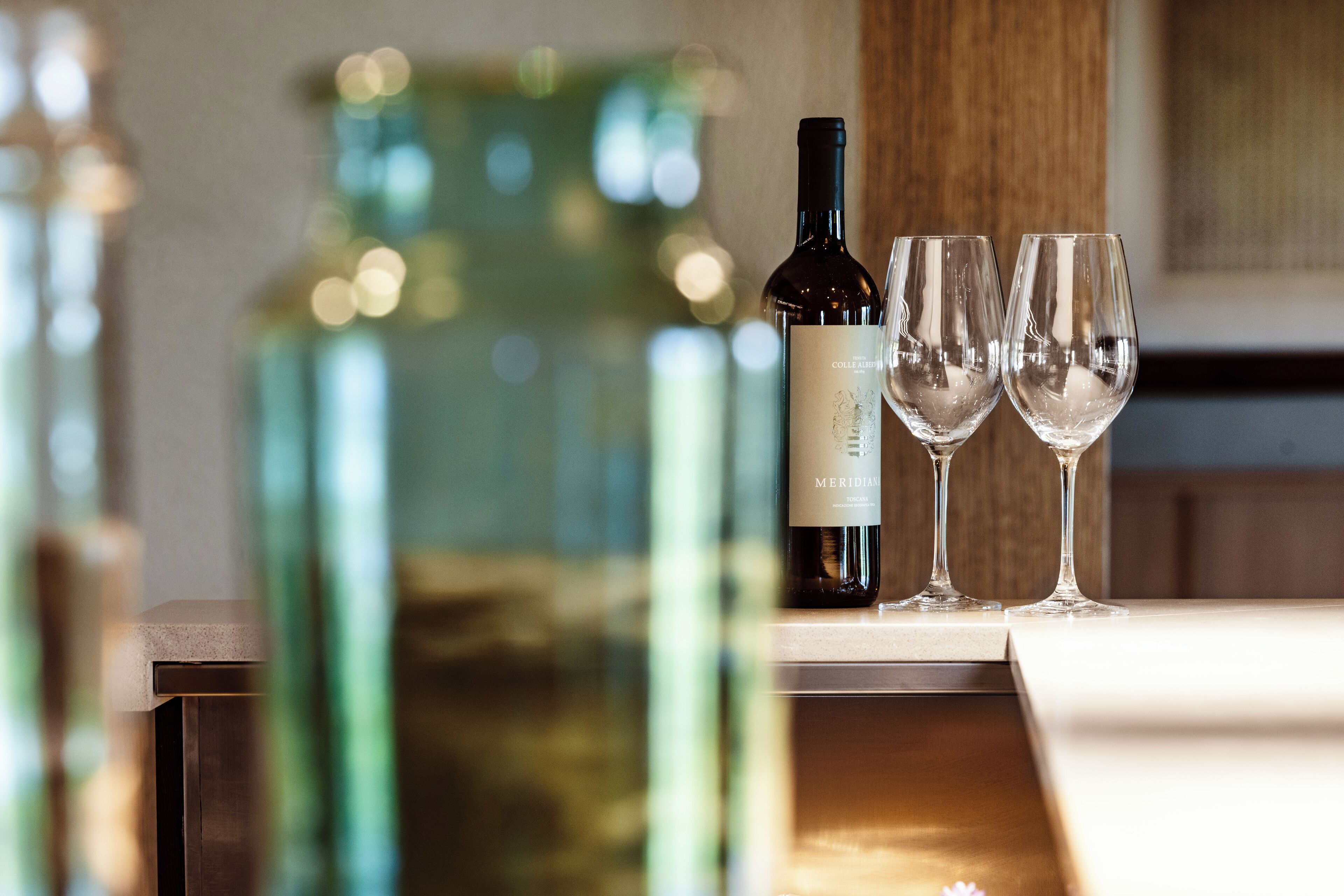 A bottle of Meridien wine and two empty wine glasses on a table with a blurred background.