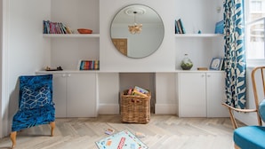 A room with a white cabinet, a round mirror, a wicker basket, and a blue chair. - Oyster Shore -  a Bloom Stays holiday let that sleeps 8 guests  in 3 bedrooms (Whitstable)