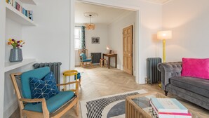 A living room with a sofa, a chair, a coffee table, and a lamp. There is a bookshelf and a radiator in the background. - Oyster Shore -  a Bloom Stays holiday let that sleeps 8 guests  in 3 bedrooms (Whitstable)