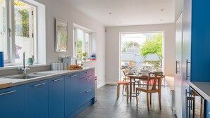 A modern kitchen with blue cabinets, a large window, and a dining area with a table and chairs. - Oyster Shore -  a Bloom Stays holiday let that sleeps 8 guests  in 3 bedrooms (Whitstable)
